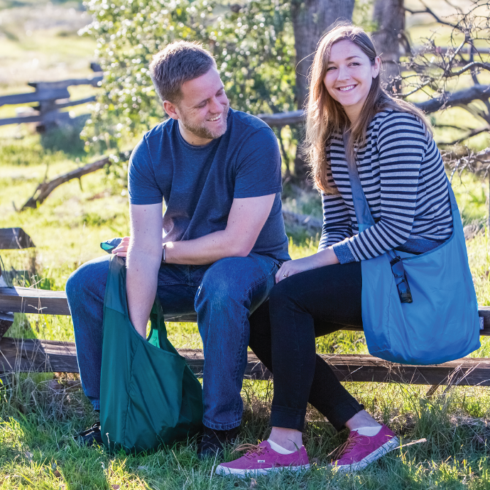 two people sitting on a fence each with a Chicobag Sling rePETe Cross Body Messenger Tote