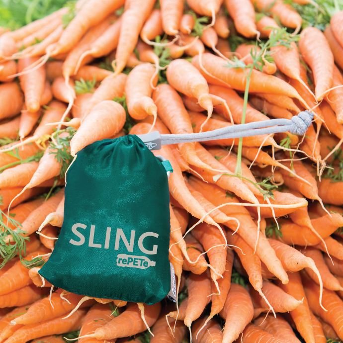 Coral colored Chicobag Sling rePETe eco friendly cross body reusable washable tote bag on top of a pile of carrots