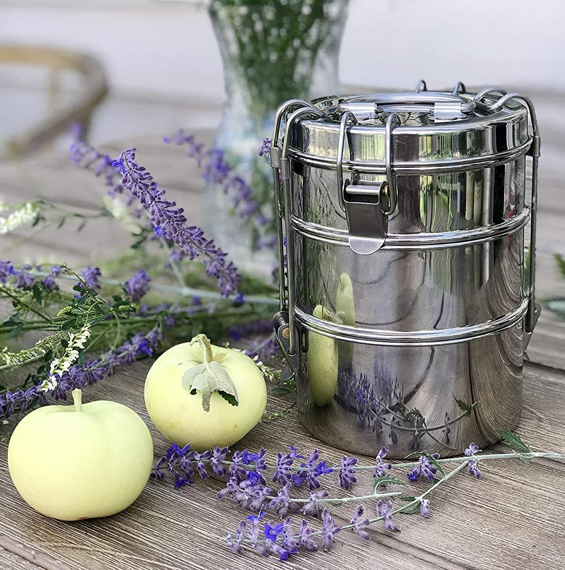 To-Go Ware 3 tier stainless steel tiffin on a table next to flowers and fruit